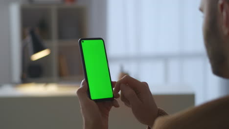 Der-Mann-Nutzt-Ein-Modernes-Smartphone-Mit-Grünem-Bildschirm-Und-Sitzt-Zu-Hause,-Nutzt-Soziale-Netzwerke-Und-Online-Shops-Und-Surft-Per-Mobiltelefon-Im-Internet,-Nahaufnahme